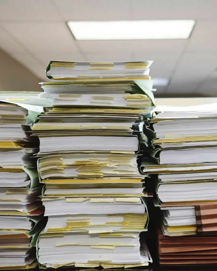 Tall stacks of client files and folders waiting to be processed in an office
