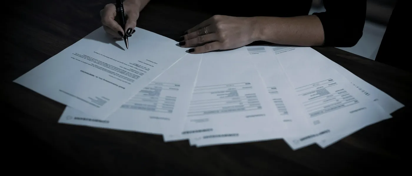 An accountant's hands with a pen, checking a fanned-out set of printed financial documents